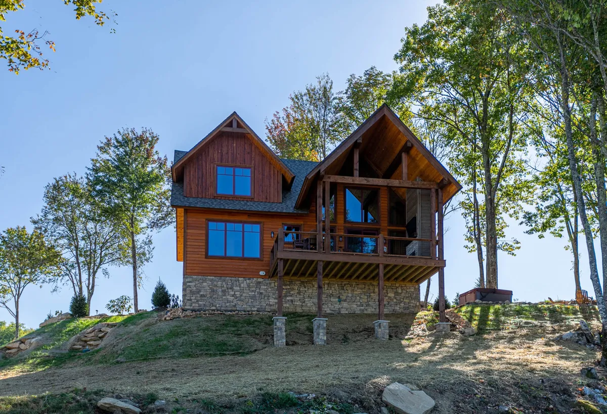 This image displays the exterior of the home, focusing on a spacious deck area framed by large windows and surrounded by serene forest. The deck provides ample space for outdoor relaxation and gatherings, perfectly set up for enjoying mountain air and scenic sunset views.