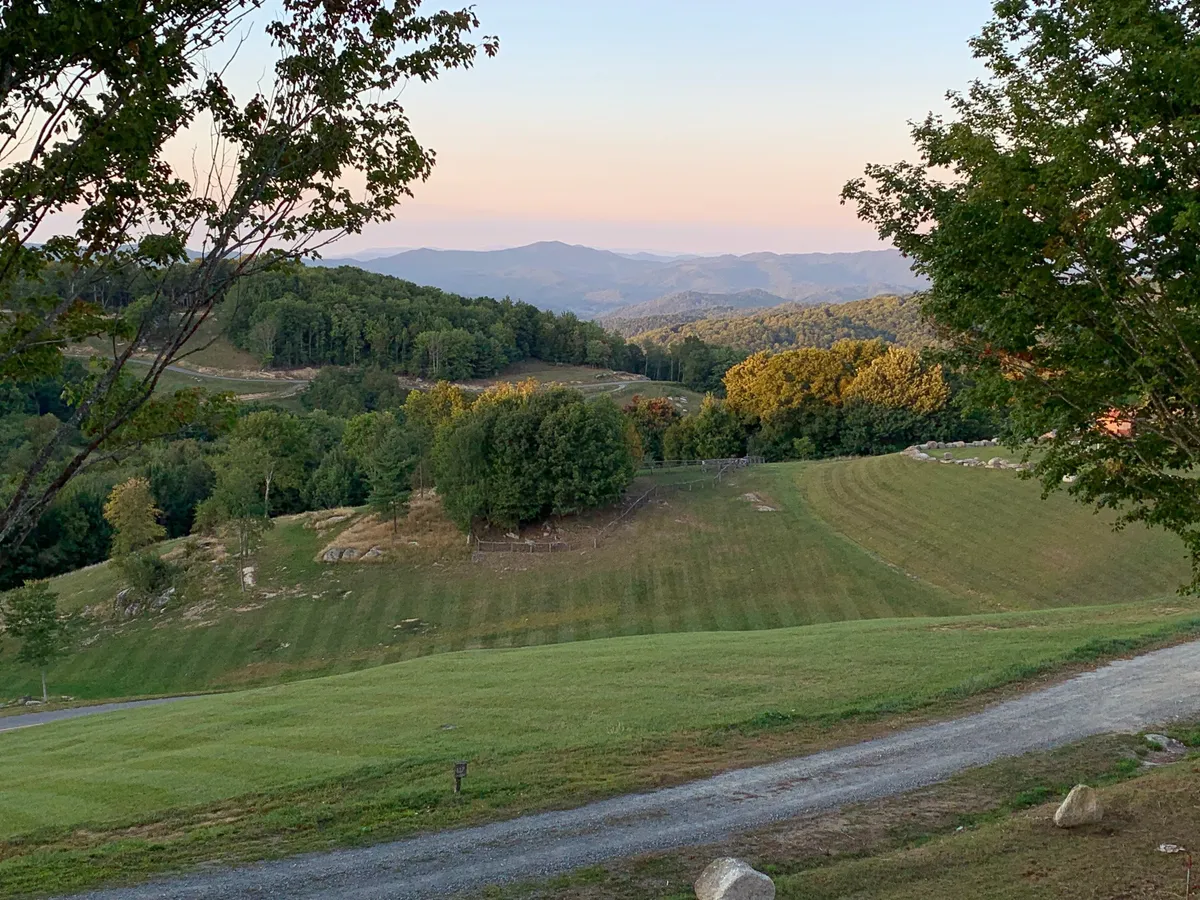 This view showcases rolling hills, distant mountains, and a gravel path winding through lush greenery, offering a sense of the surrounding landscape. The scene invites exploration, hiking, and outdoor adventures.