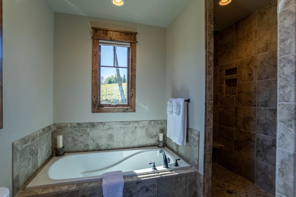 A tranquil spa-inspired bathroom with a soaking tub, a separate shower area, and a window offering a view of nature. The bathroom is filled with soft, natural light, creating an atmosphere of relaxation and indulgence.