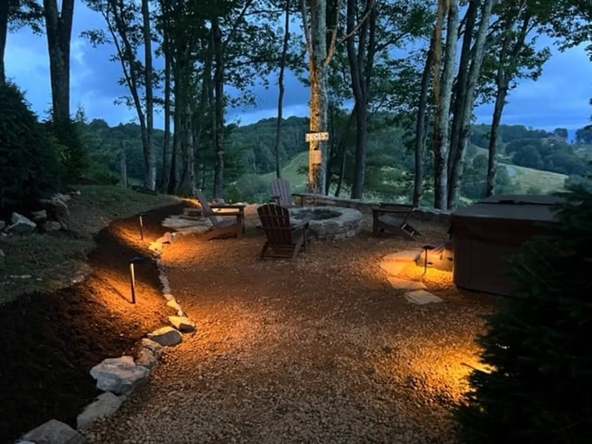 A cozy fire pit area surrounded by Adirondack chairs and softly lit pathways, set amidst tall trees. The mood is warm and inviting, perfect for gathering after a day on the trails or slopes.