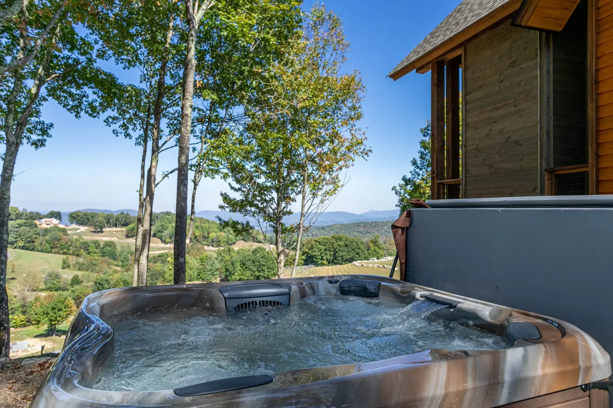 A serene exterior view of the hot tub nestled among trees, with sweeping mountain vistas in the background. The deck space is inviting for morning coffee or an evening soak, and the peaceful, pet-friendly atmosphere is evident.