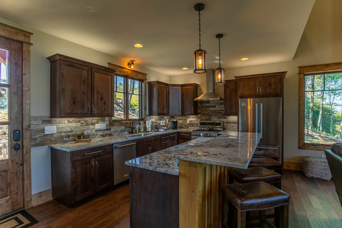 A modern kitchen with granite countertops, wooden cabinets, stainless steel appliances, and large windows providing natural light. The kitchen is well-equipped, inviting culinary adventures and comfortable gatherings, while the vista through the windows enhances the sense of space.