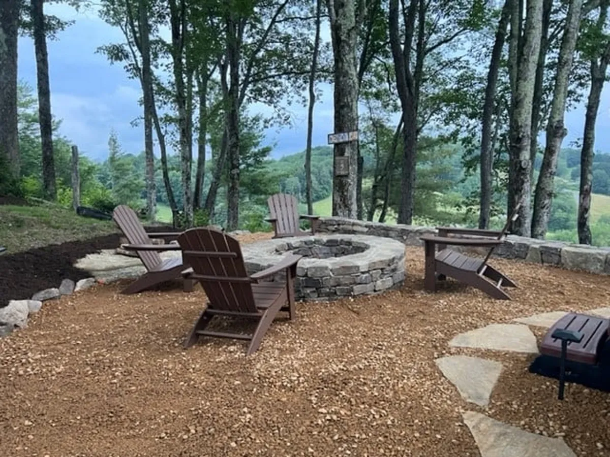 A cozy outdoor fire pit area with Adirondack chairs arranged under tall trees, set up for evenings spent sharing stories, stargazing, or savoring a glass of wine by the fire in a communal yet private forest enclave.