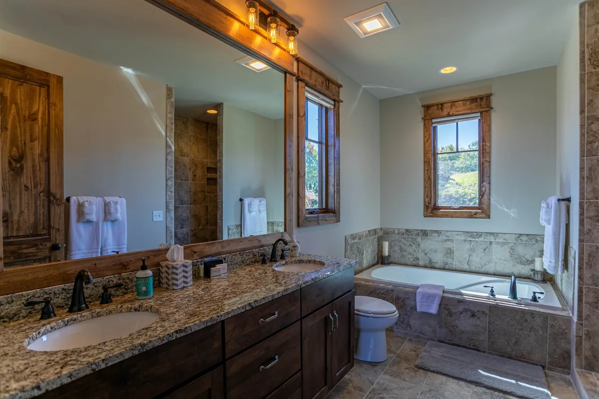 A modern bathroom featuring a double sink vanity, large mirror, inviting bathtub, and abundant natural light streaming in through the windows. The space feels bright and soothing—ideal for morning routines and evening relaxation.