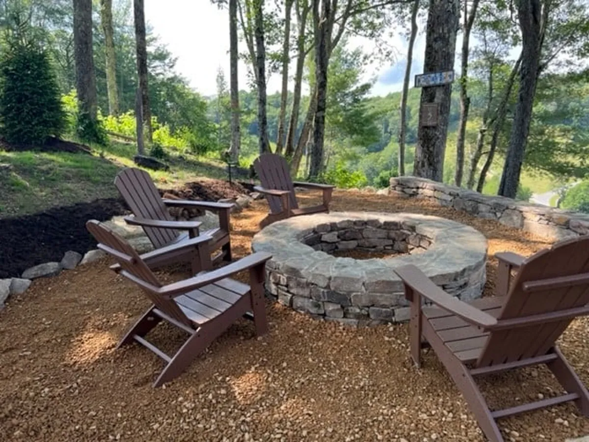 This exterior image shows a fire pit surrounded by Adirondack chairs, nestled among tall trees. The scene is set for an evening gathering, suggesting activities like roasting marshmallows, sharing stories, and enjoying the outdoors together.